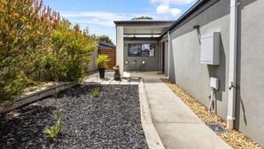 Ein modernes Haus mit Betonweg, einem kleinen Garten mit Mulch und Pflanzen sowie Gartenmöbeln.