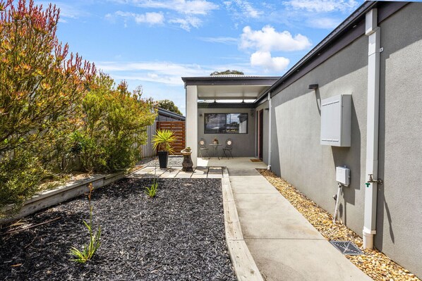 A modern house with a concrete pathway, a small garden with mulch and plants, and outdoor furniture. - Haylock Haven: Relax, explore, and feel right at home (Paynesville)