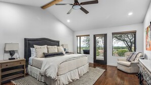 A bedroom with a large bed, a nightstand, a chair, and a view through a door. - 5BR Luxury Home w/ Pool & Wrap-around Porch (Glen Rose)
