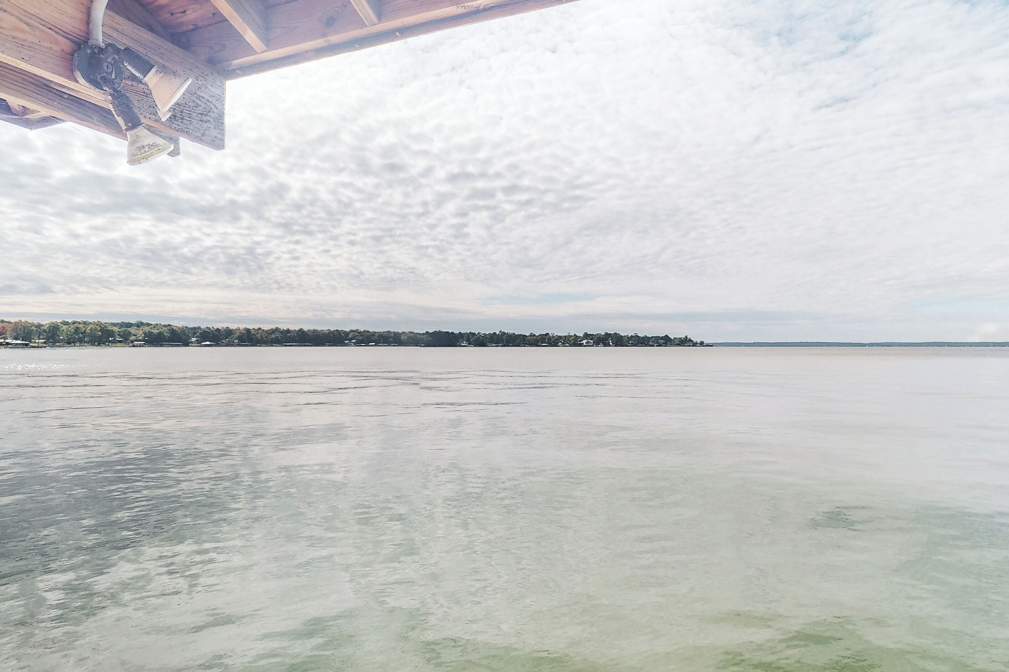 A view of a frozen lake with a wooden structure on the left and a distant shoreline with trees and buildings.