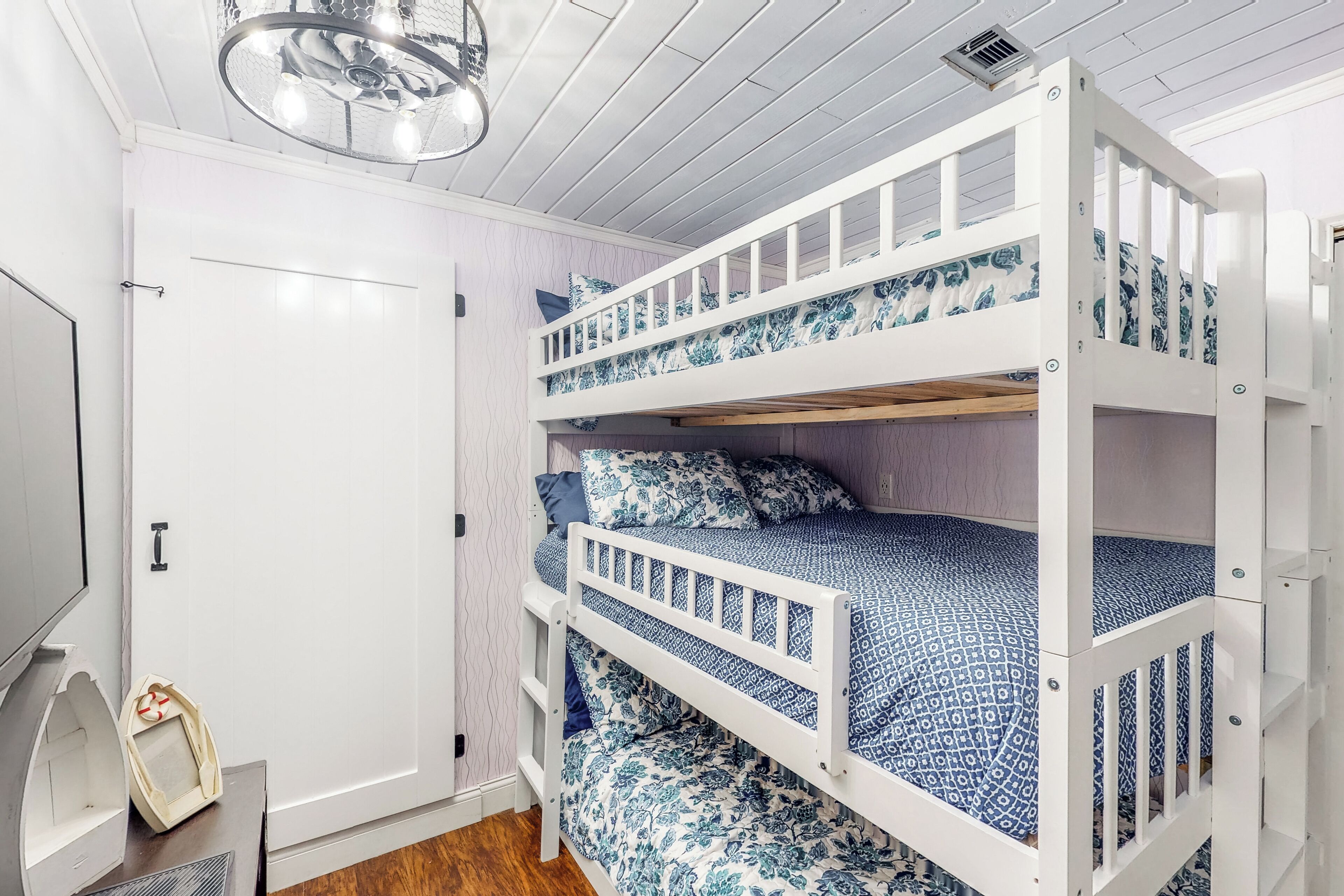 Una cama litera con ropa de cama de diseño azulado, una puerta blanca y un ventilador de techo.