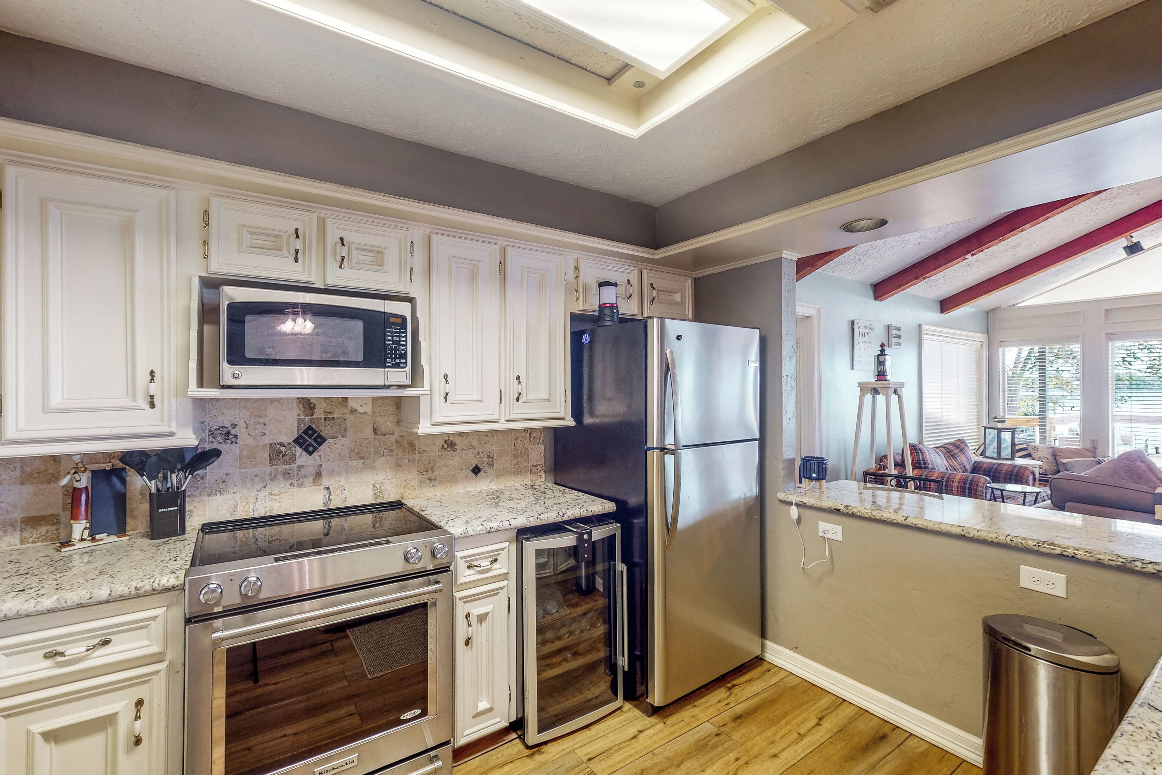 A modern kitchen with white cabinets, stainless steel appliances, and a wooden floor.