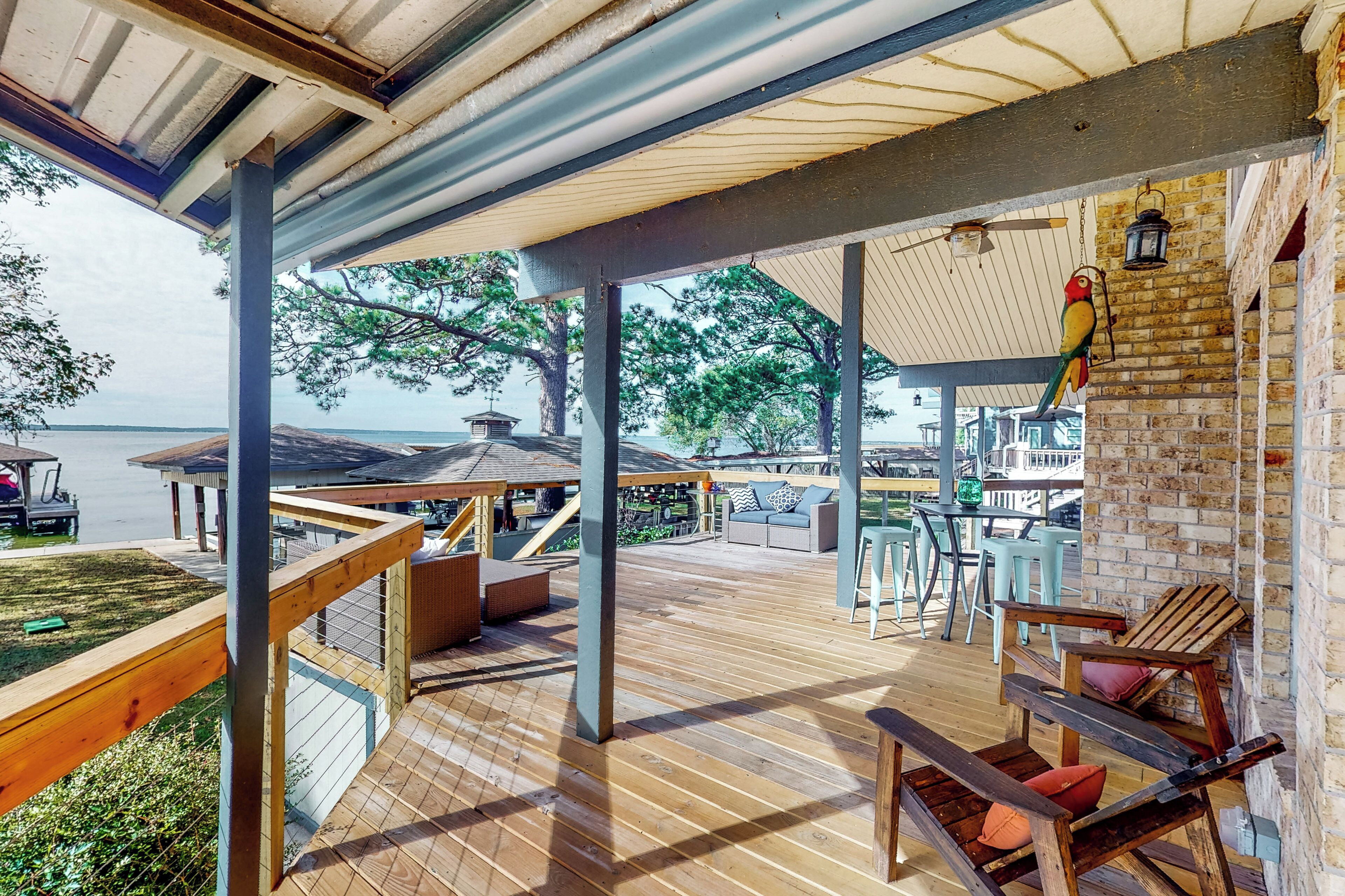 A wooden deck with outdoor seating, a brick wall, and a view of the water.
