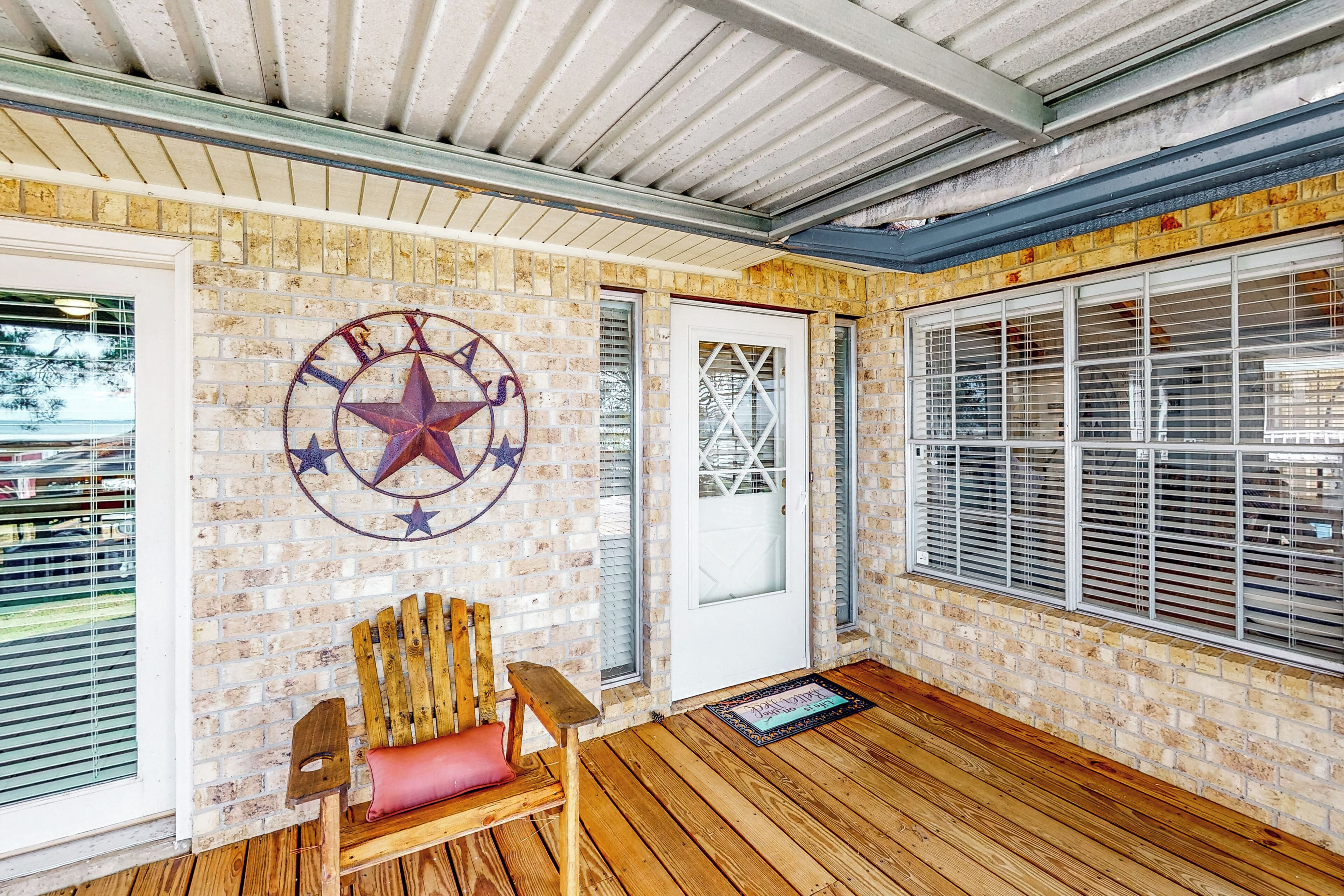 A covered porch with a wooden bench, a Texas state emblem on the wall, and a door with a decorative glass window.