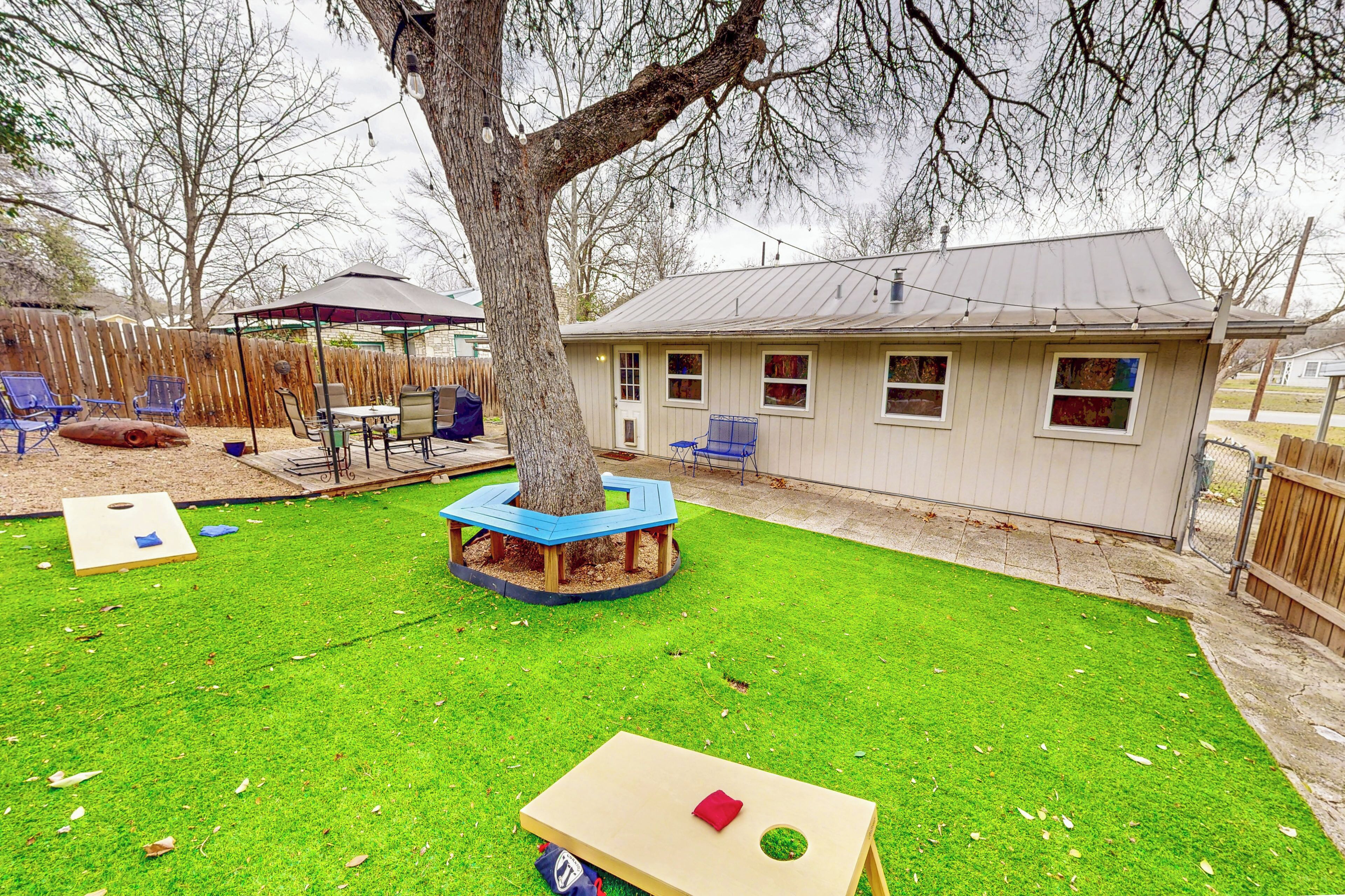 A backyard with a wooden play table, a blue play structure, and a house in the background.