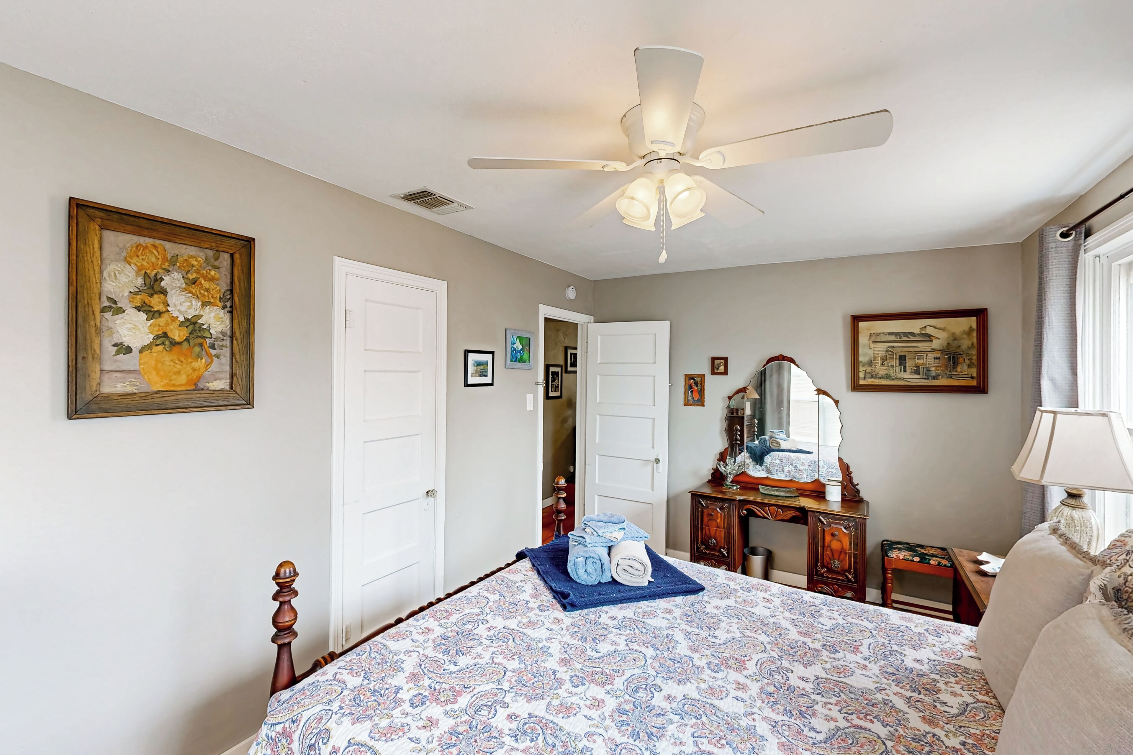 Une chambre à coucher avec un lit, un ventilateur de plafond, une commode et un tableau accroché au mur.