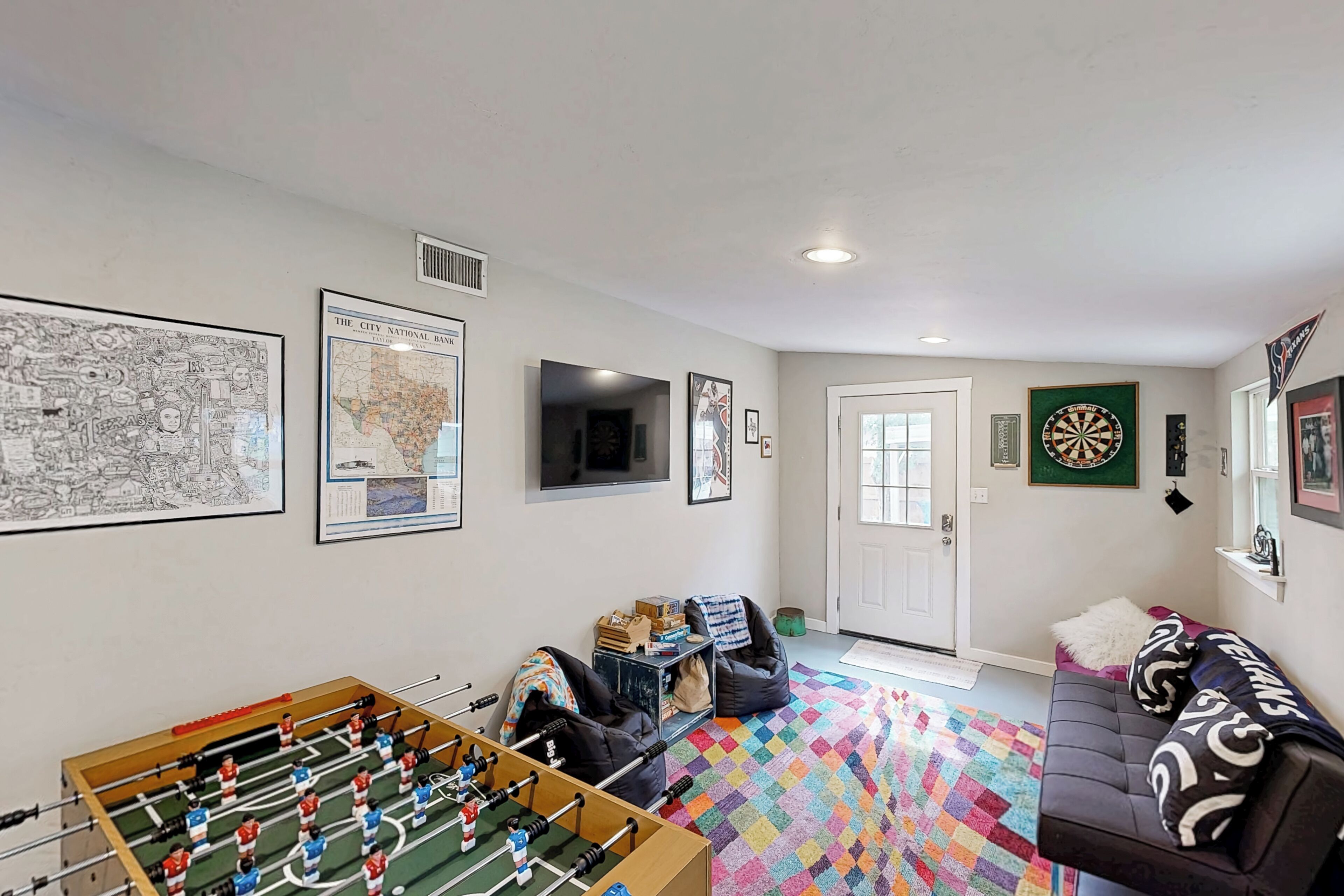 A living room with a foosball table, a couch, a dartboard, and various framed pictures on the walls.