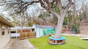 Ein Garten mit Baum, Spielhaus und umzäunter Fläche.