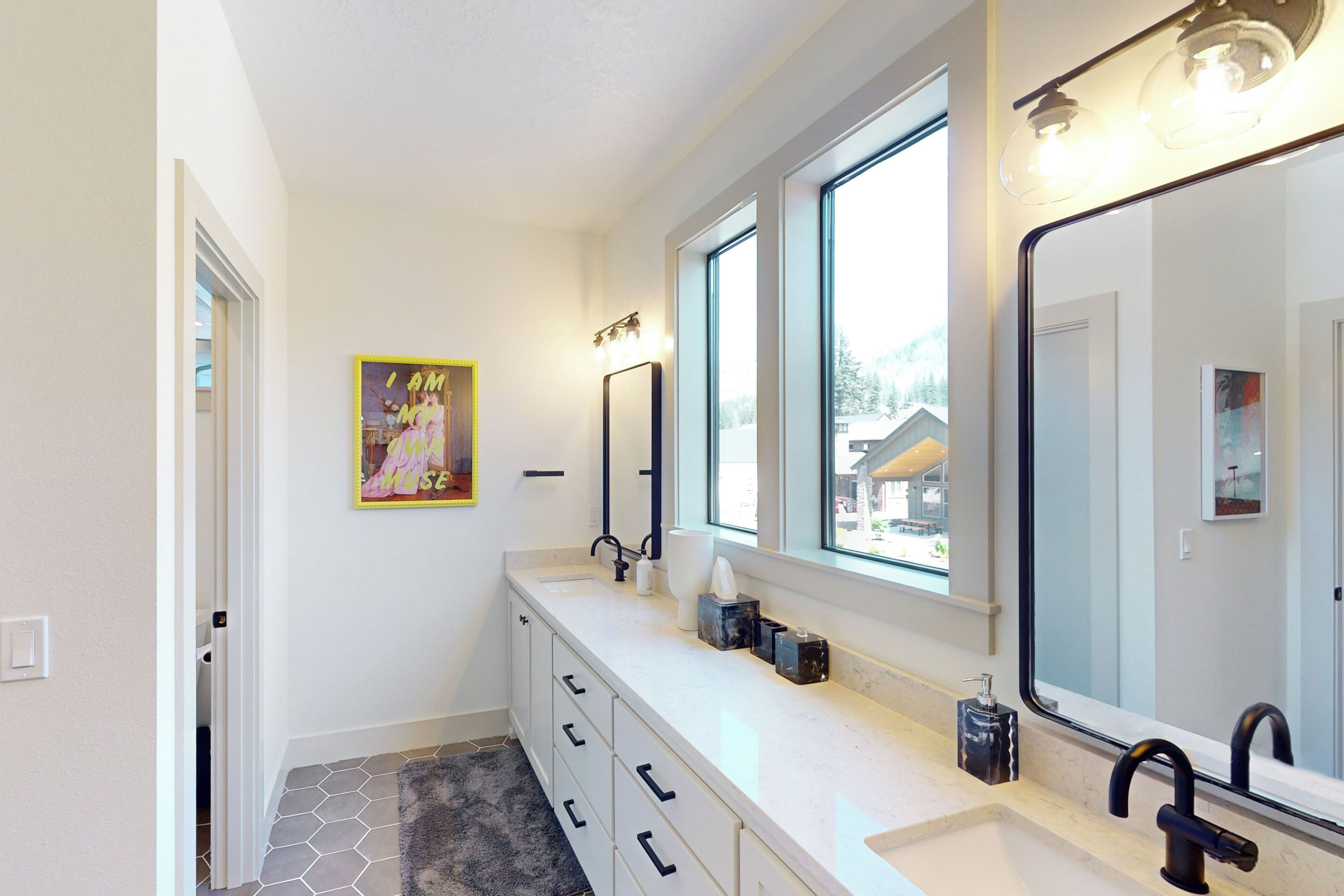 A modern bathroom with a large mirror, two sinks, and a window.