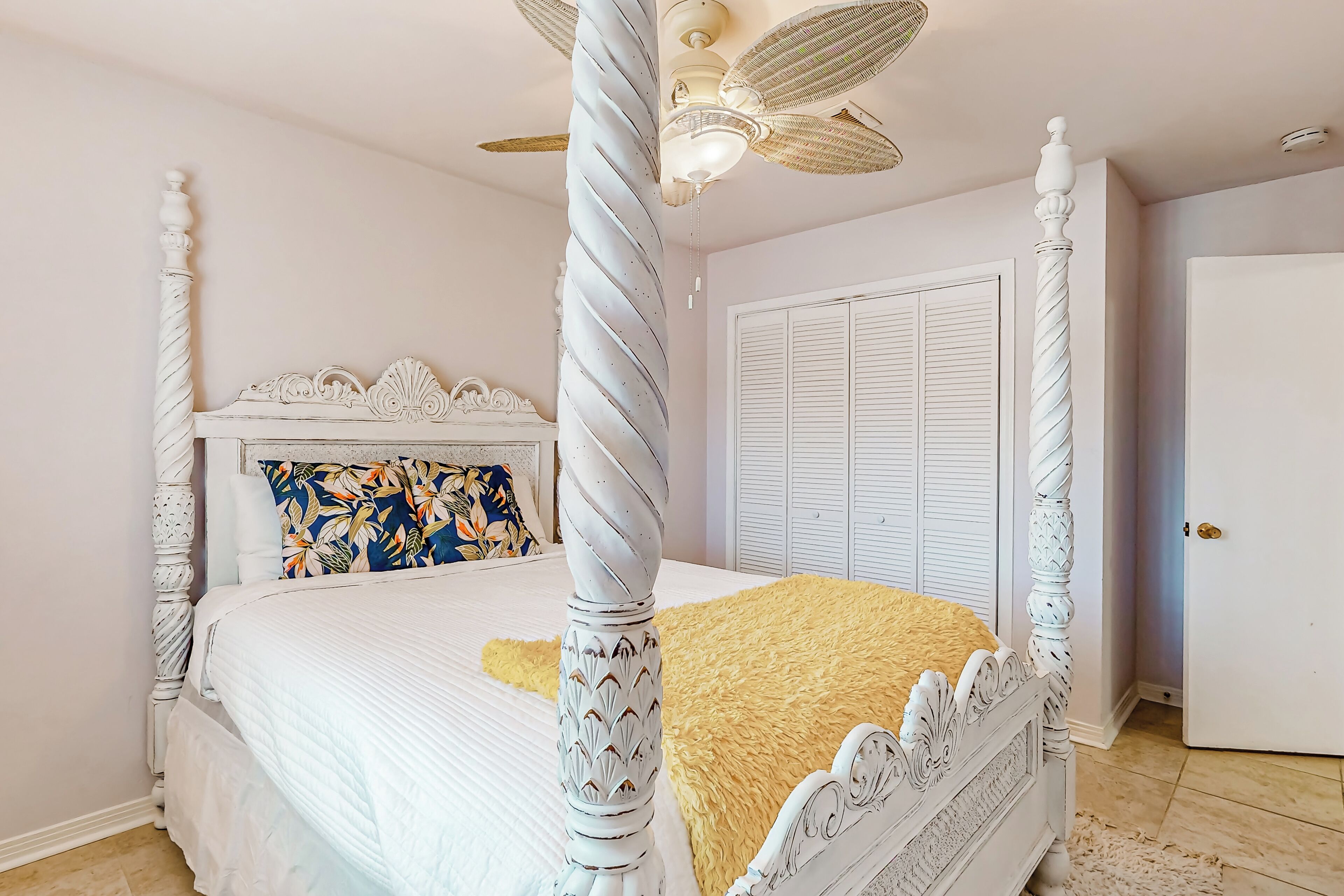 A four-poster bed with a decorative headboard, a ceiling fan, and a white wardrobe in a bedroom.
