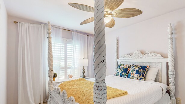 A four-poster bed with a white headboard, a yellow throw blanket, and a floral pillow.