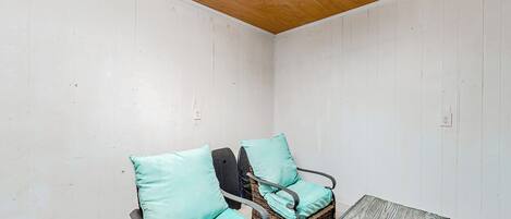 A corner room with two wicker chairs with teal cushions, a small table, and a wooden ceiling.