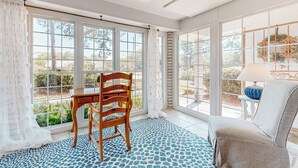 A sunroom with a wooden table and chairs, large windows, and a patterned floor.