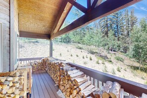 A wooden deck with stacked firewood and a view of a forested hillside. - 3 BR Cabin w/ Hot Tub, Large Deck & Wifi (Jefferson)