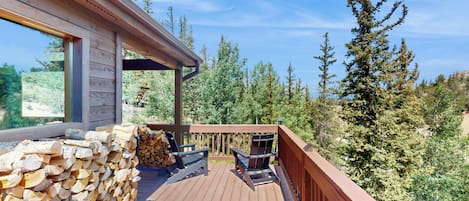 A wooden deck with a stone wall, two Adirondack chairs, and a grill.
