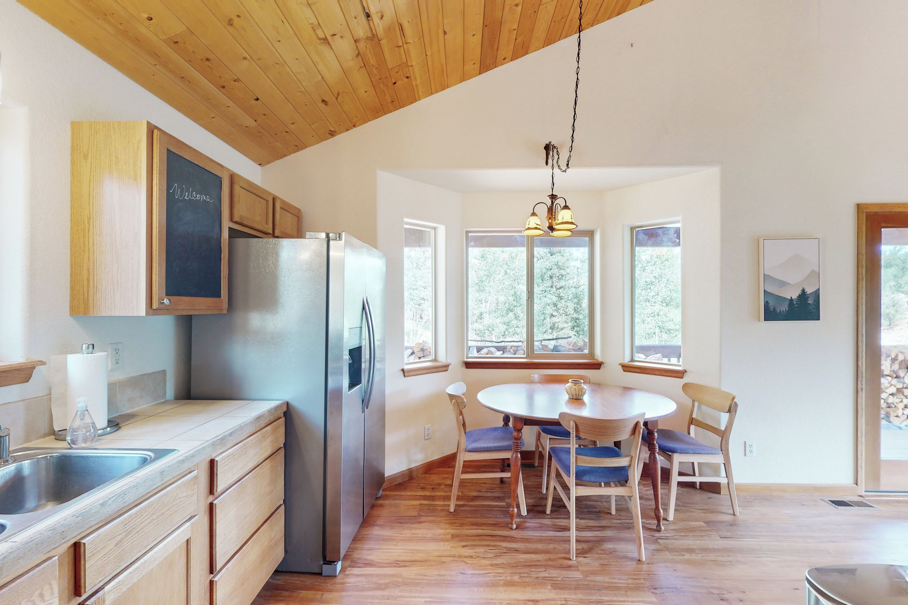 A kitchen with wooden cabinets, a stainless steel refrigerator, a sink, and a dining area with a round table and chairs.