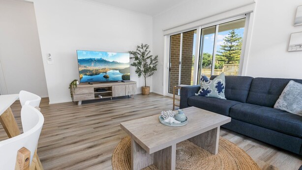 Ein modernes Wohnzimmer mit einem Flachbildfernseher, einem dunkelblauen Sofa, einem Holztisch und einem gewebten Teppich.