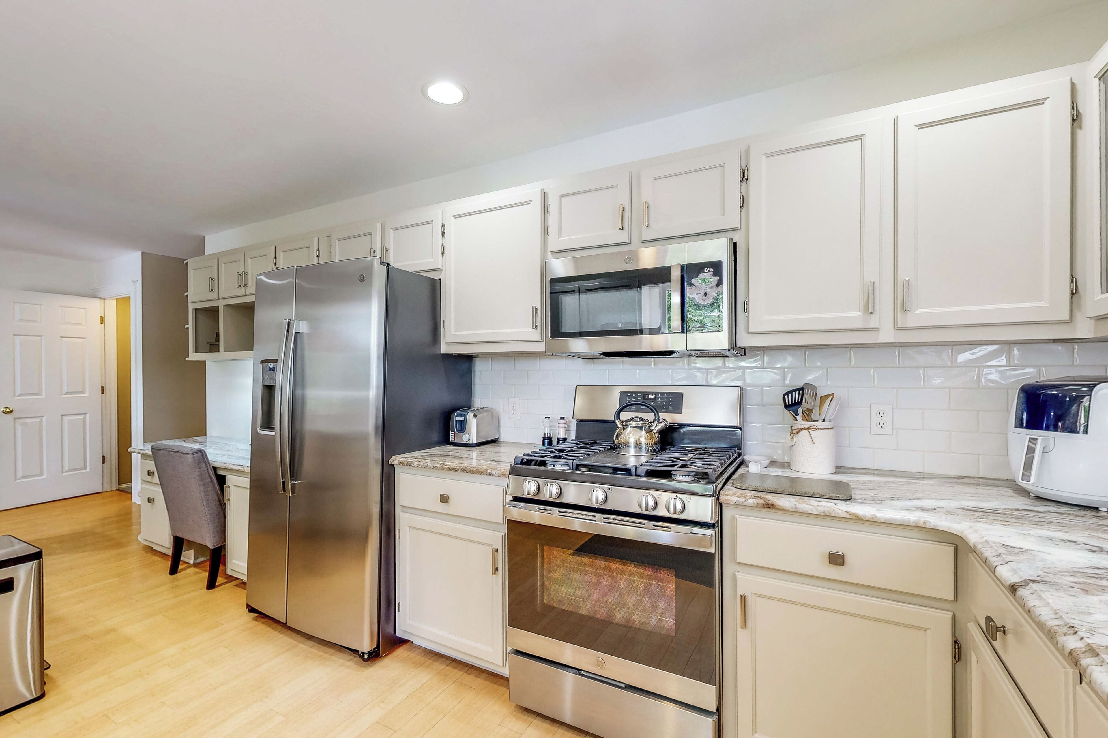 A kitchen with white cabinets, a stainless steel refrigerator, a microwave, a stove, and a toaster.