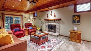 A cozy living room with a fireplace, a red armchair, a glass coffee table, and a wooden cabinet. - Salisbury Waterfront: Schumaker Pond Paradise! (Salisbury)