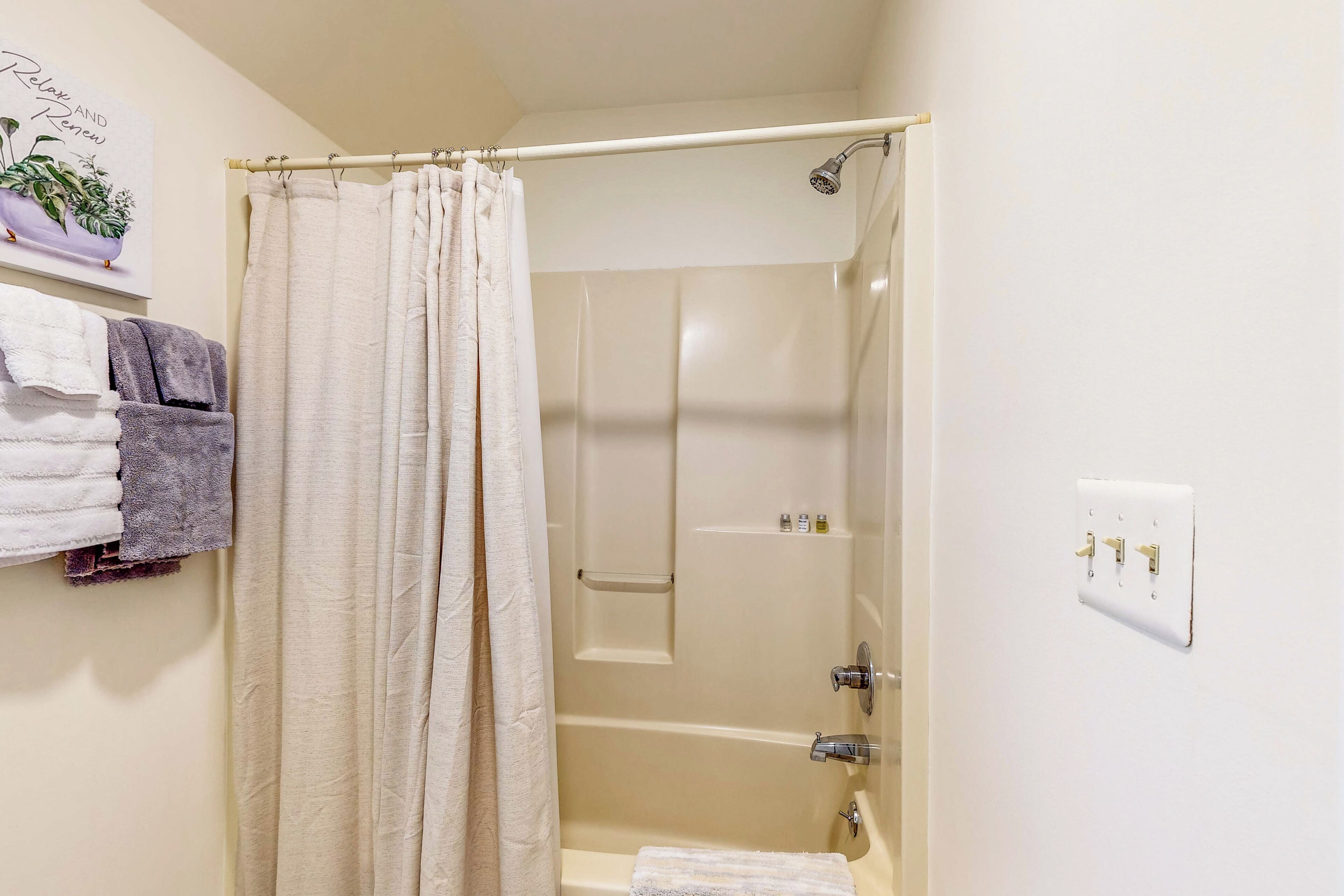 A bathroom with a shower, a towel rack with towels, and a wall-mounted light switch.