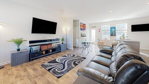 Un salon moderne comprenant un canapé en cuir, un téléviseur à écran plat, un coin repas avec une table et des chaises, et un coin cuisine avec un évier et des placards.