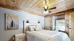 A bedroom with a wooden ceiling, a bed with white bedding, a nightstand, a painting on the wall, and a window with curtains. - Charming Home w/ Patio Near Downtown! (Morganton)