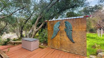Una terraza de madera con un cerco de madera que presenta un diseño alado, un jacuzzi y un muro de piedra.