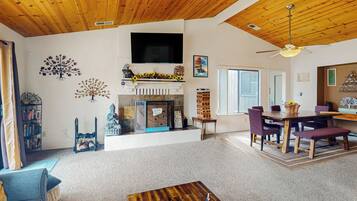 A spacious living room with a fireplace, wooden ceiling, and a dining area with a table and chairs.