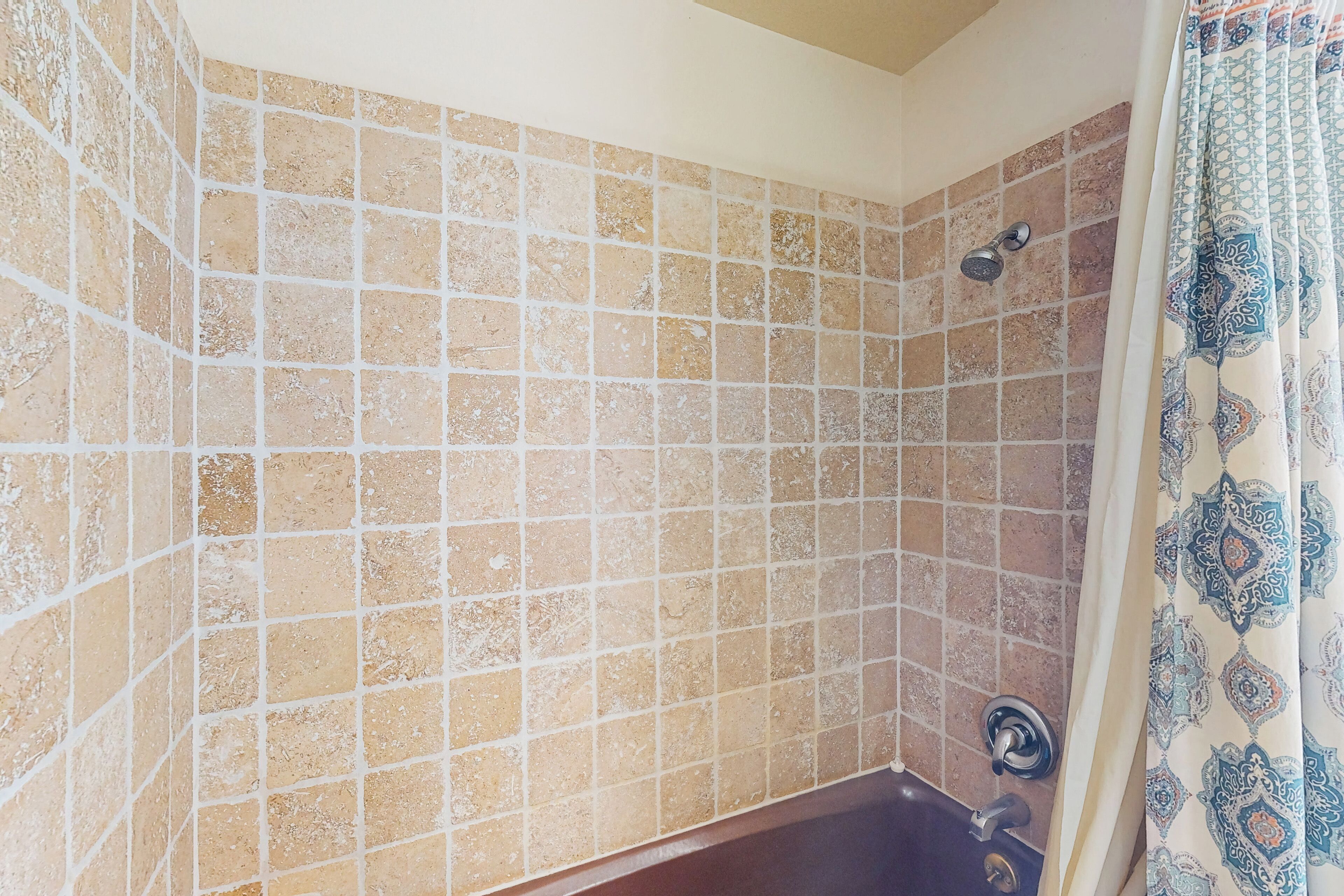 Een badkamer met behang van beige en bruine tegels, een douche met een handdouche en een decoratief gordijn.