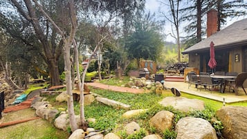 A rustic outdoor area with a wooden deck, stone pathway, and a dining area with outdoor furniture.
