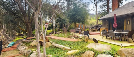 Un espace extérieur rustique doté d’une terrasse en bois, d’un chemin en pierre et d’un coin repas avec du mobilier d’extérieur.