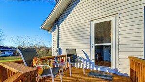Una terraza de madera con mobiliario exterior, una puerta corrediza de vidrio y vista despejada al jardín.