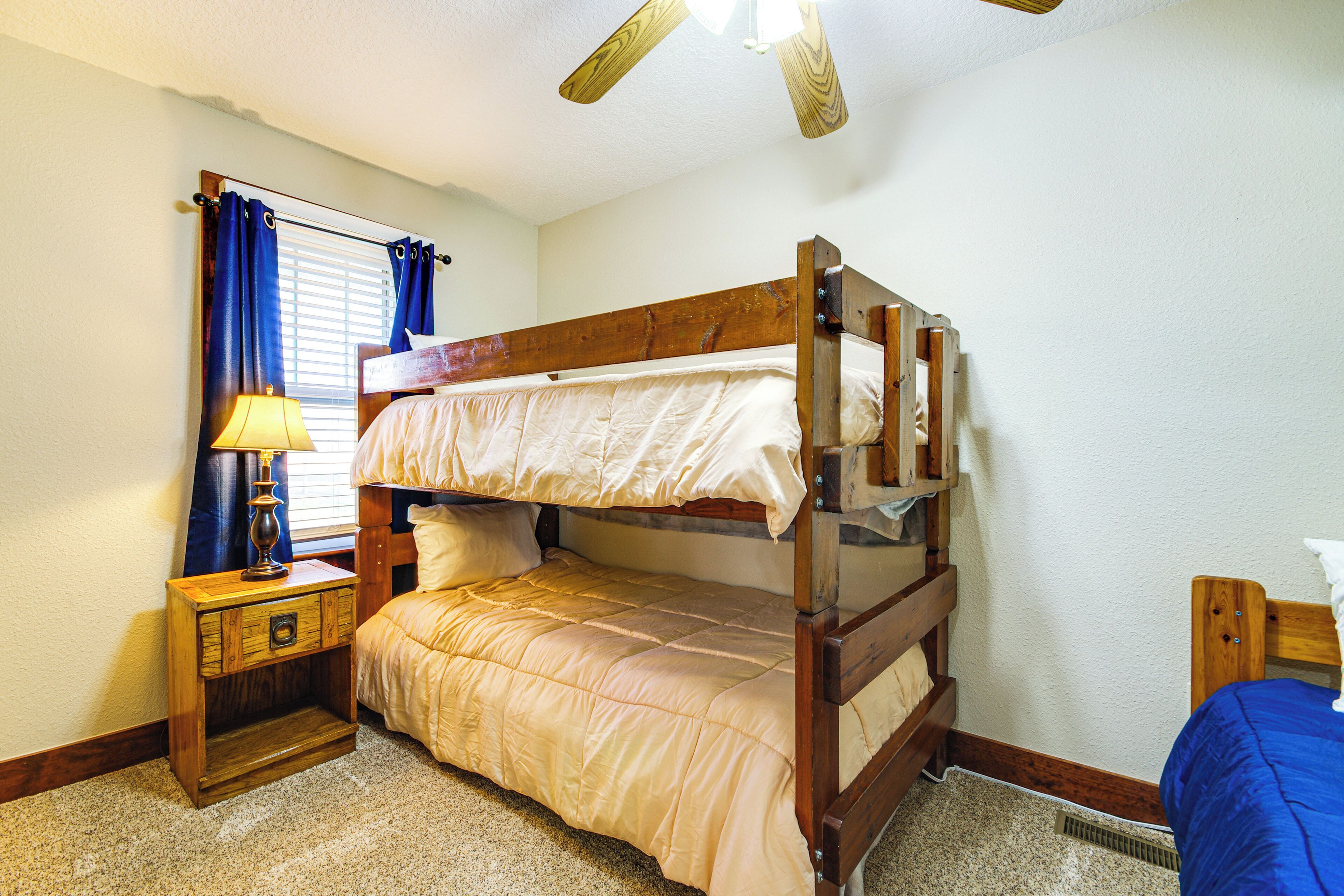A bunk bed with a wooden frame, a bedside table with a lamp, and a window with blue curtains.