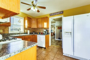 Une cuisine avec des meubles en bois, un réfrigérateur blanc, des plans de travail en granit et un ventilateur de plafond.