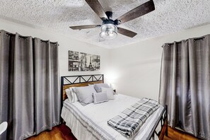A bedroom with a bed, curtains, a ceiling fan, and a wall-mounted picture.