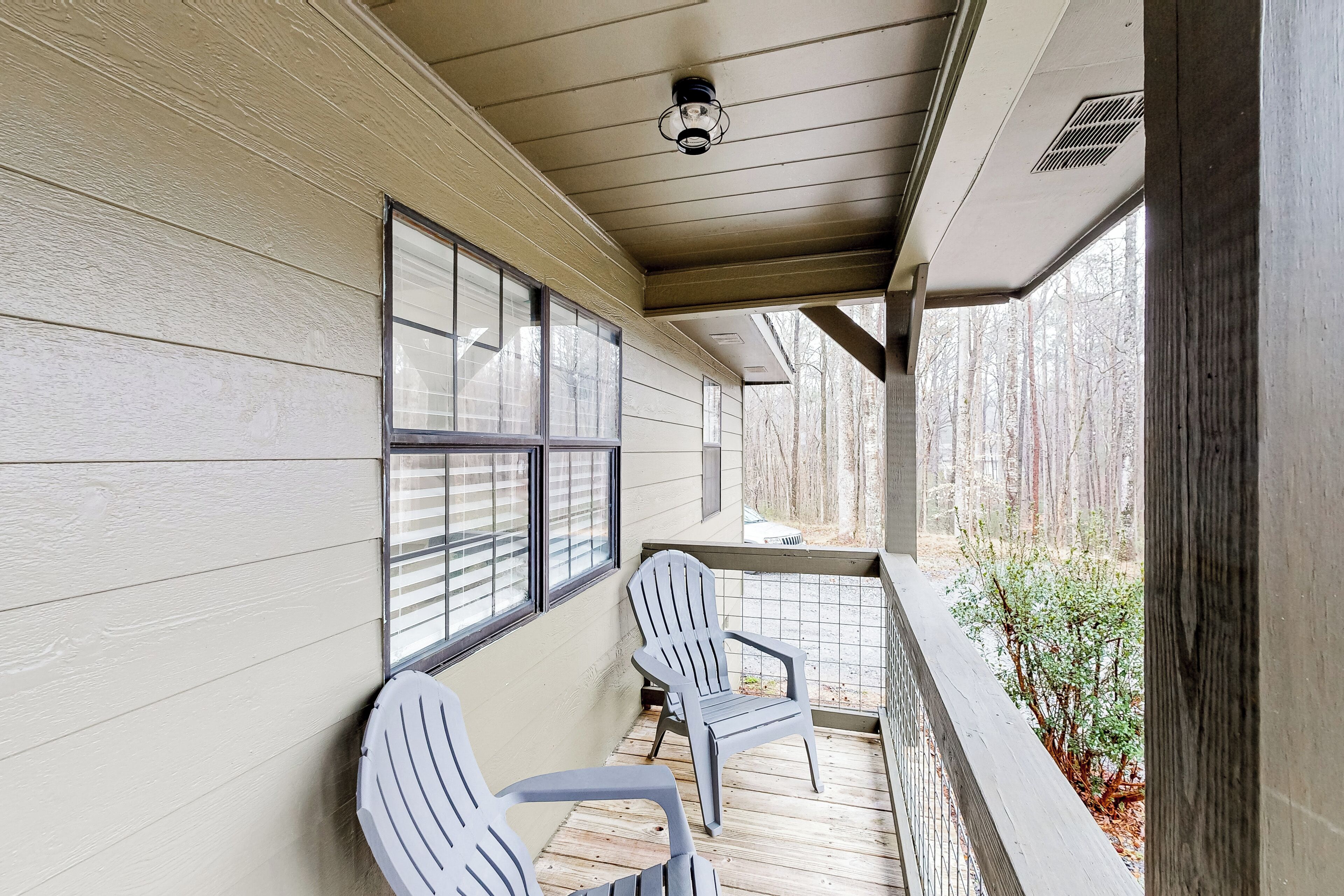 Une véranda couverte avec deux fauteuils Adirondack, un luminaire au plafond et une vue sur une zone boisée.