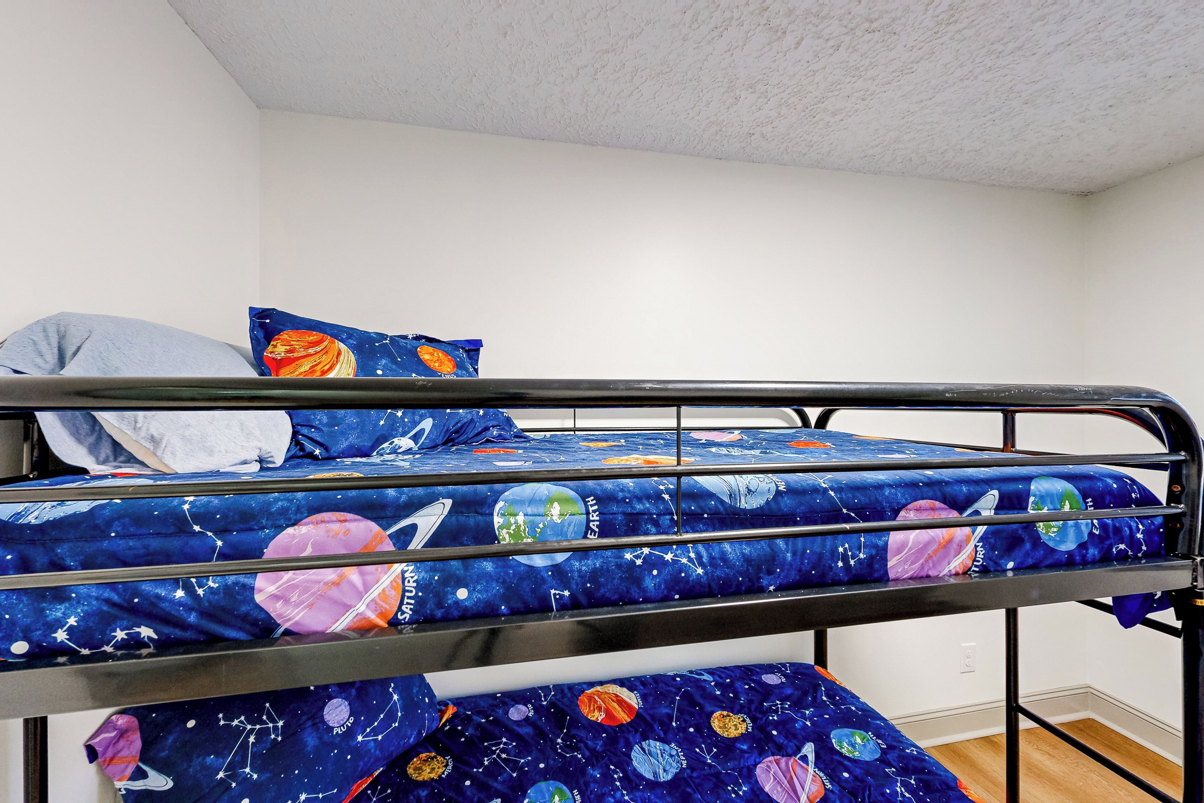 Una cama litera con un edredón de temática espacial, una almohada y una manta.