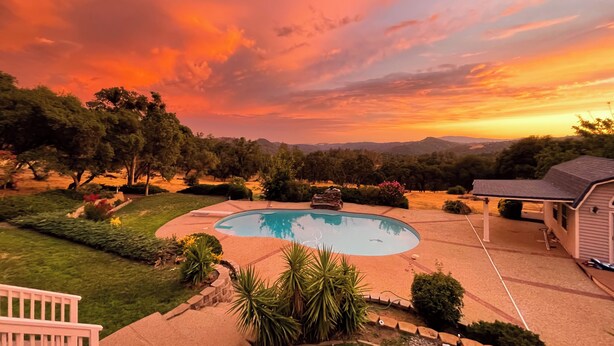 Um quintal com piscina, rodeado por gramados bem cuidados e árvores, sob um céu ao pôr do sol.