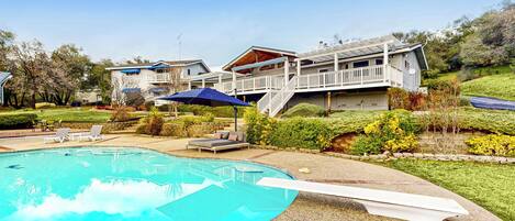 A residential property with a swimming pool, outdoor seating, and a multi-level house with a deck.