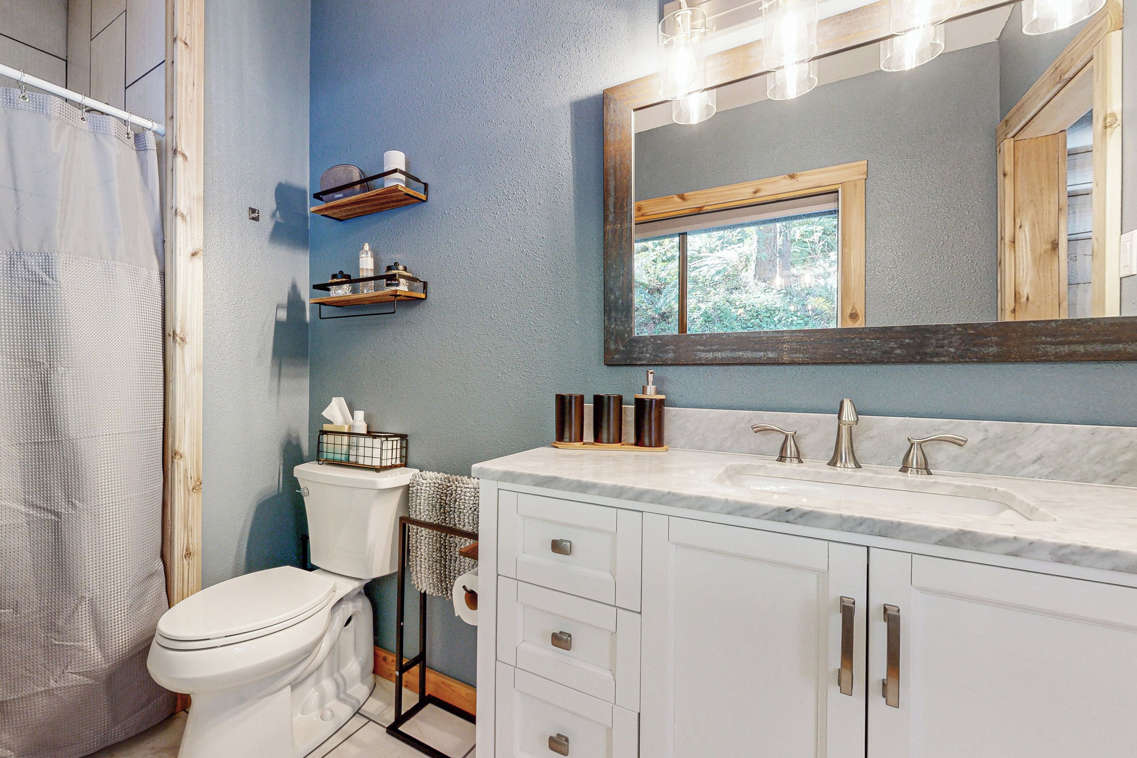 A bathroom with a white sink, a mirror, and a toilet. There are shelves above the sink and a towel rack next to the toilet.