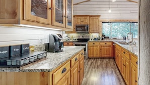 A kitchen with wooden cabinets, granite countertops, and a large window. - Kalama River View! Family-friendly Nature Escape (Kalama)