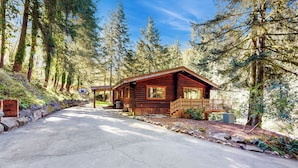 A wooden cabin with a porch, surrounded by tall trees and a clear sky. - Kalama River View! Family-friendly Nature Escape (Kalama)