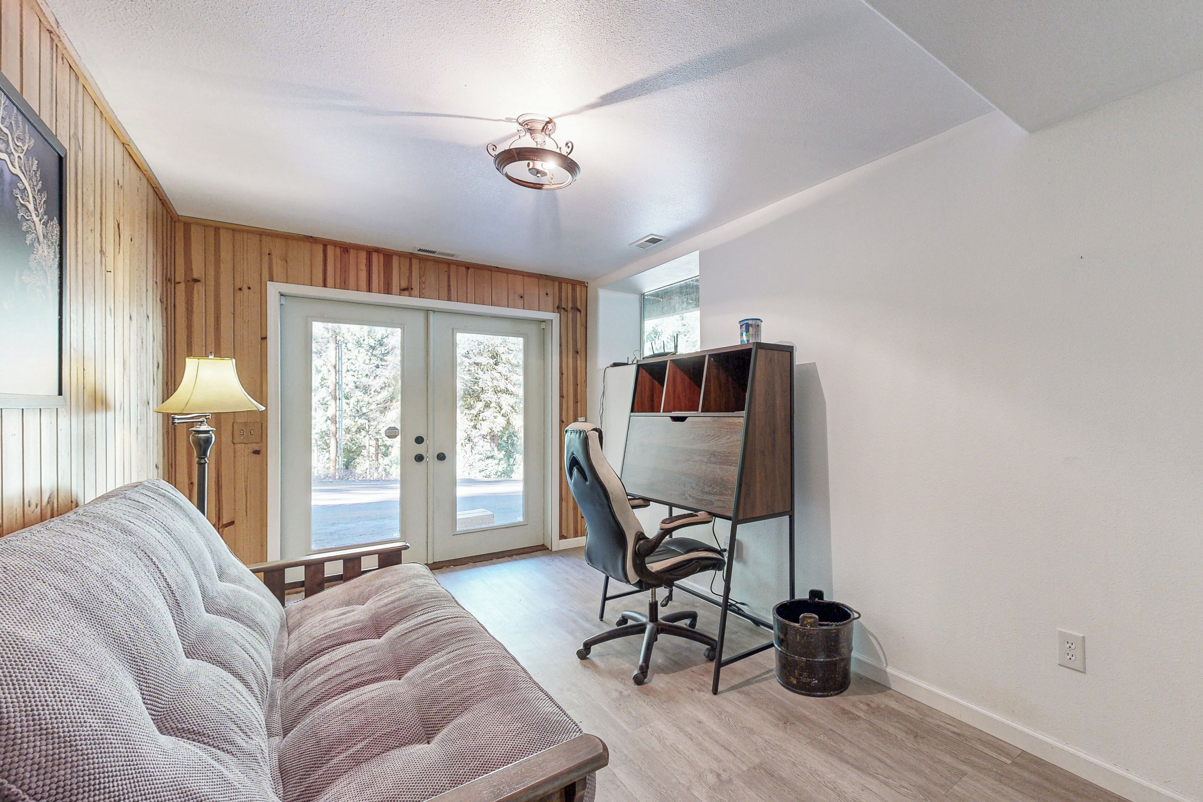 A room with a wooden paneled wall, a desk with a chair, a couch, and a lamp.