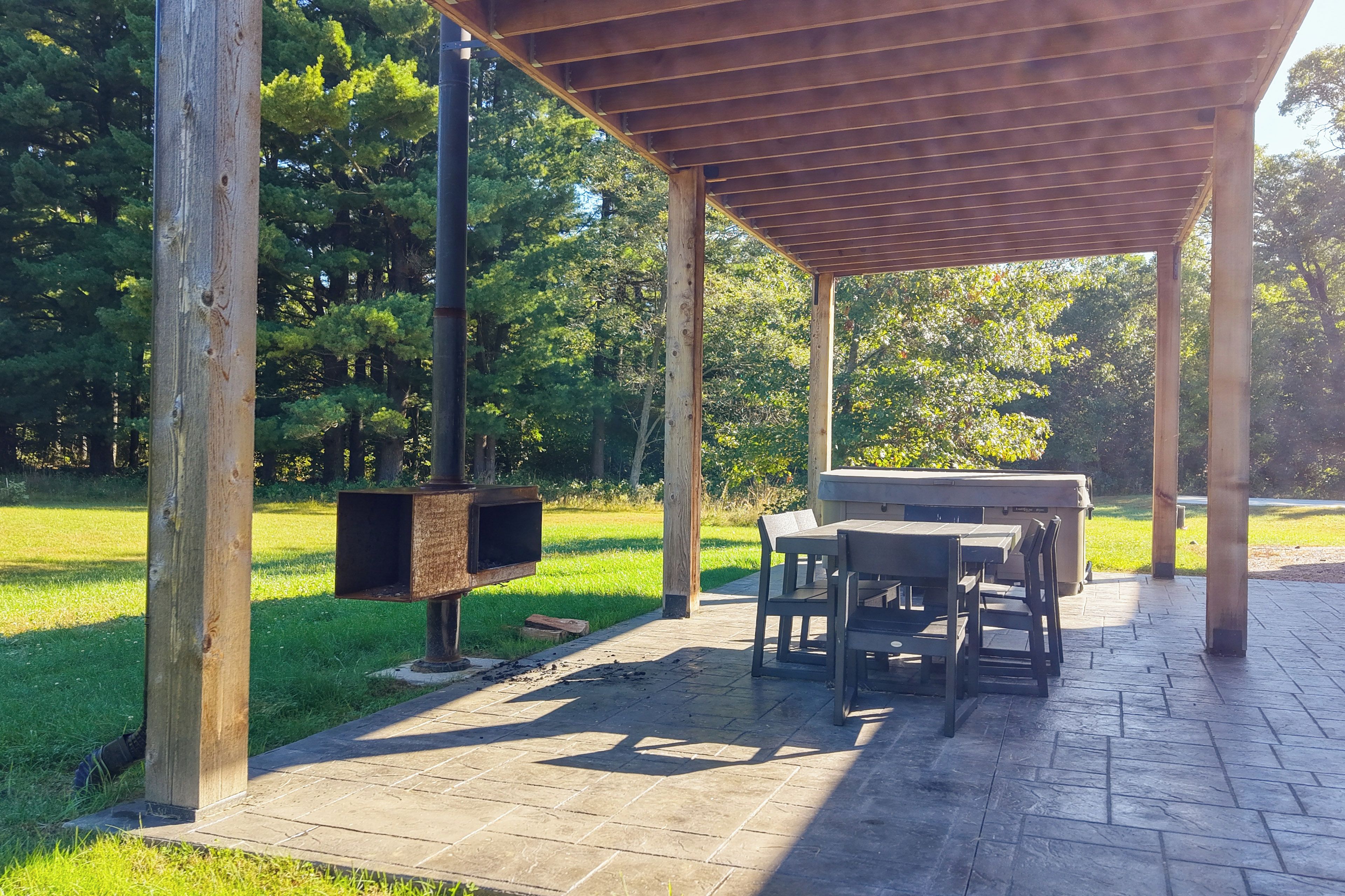 Un área de patio al aire libre con una pérgola, una parrilla y una mesa con sillas.