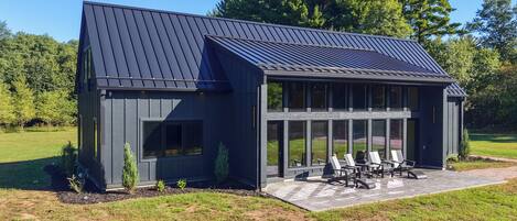 A modern building with a sloped roof, large windows, and a patio area with outdoor seating.