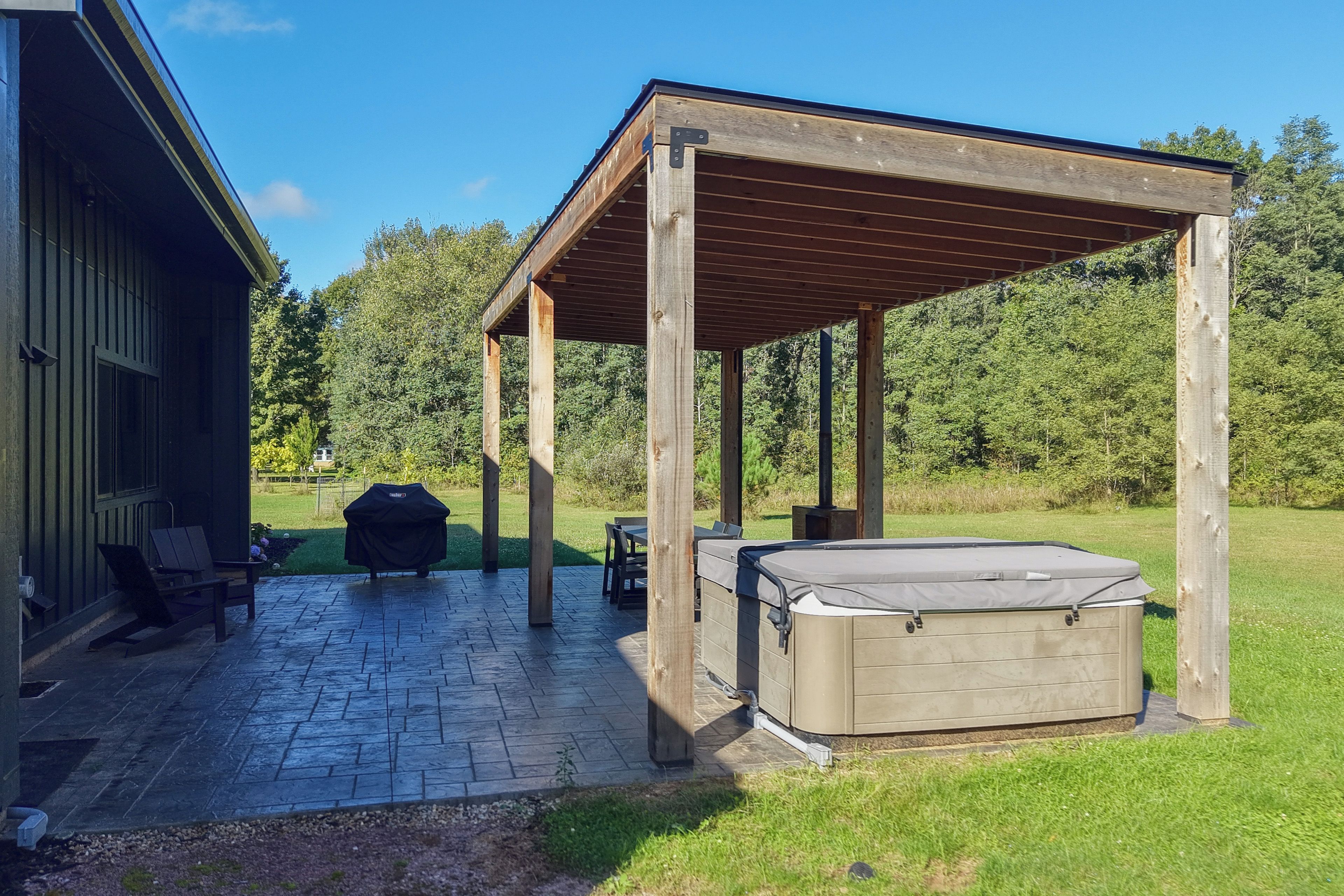 A covered patio area with a hot tub, outdoor seating, and a barbecue grill.