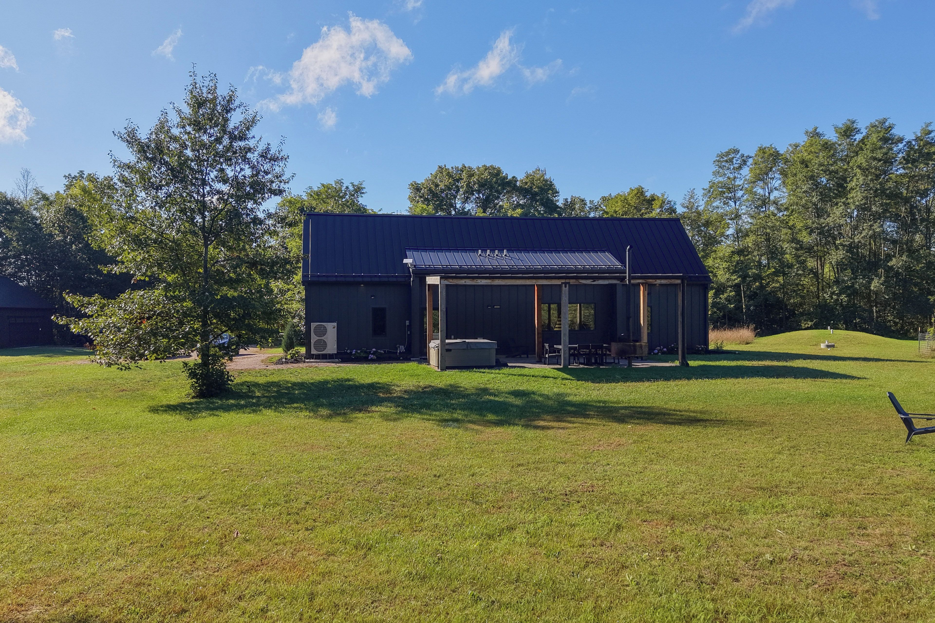 A single-story building with a covered patio area, surrounded by a grassy field and trees.
