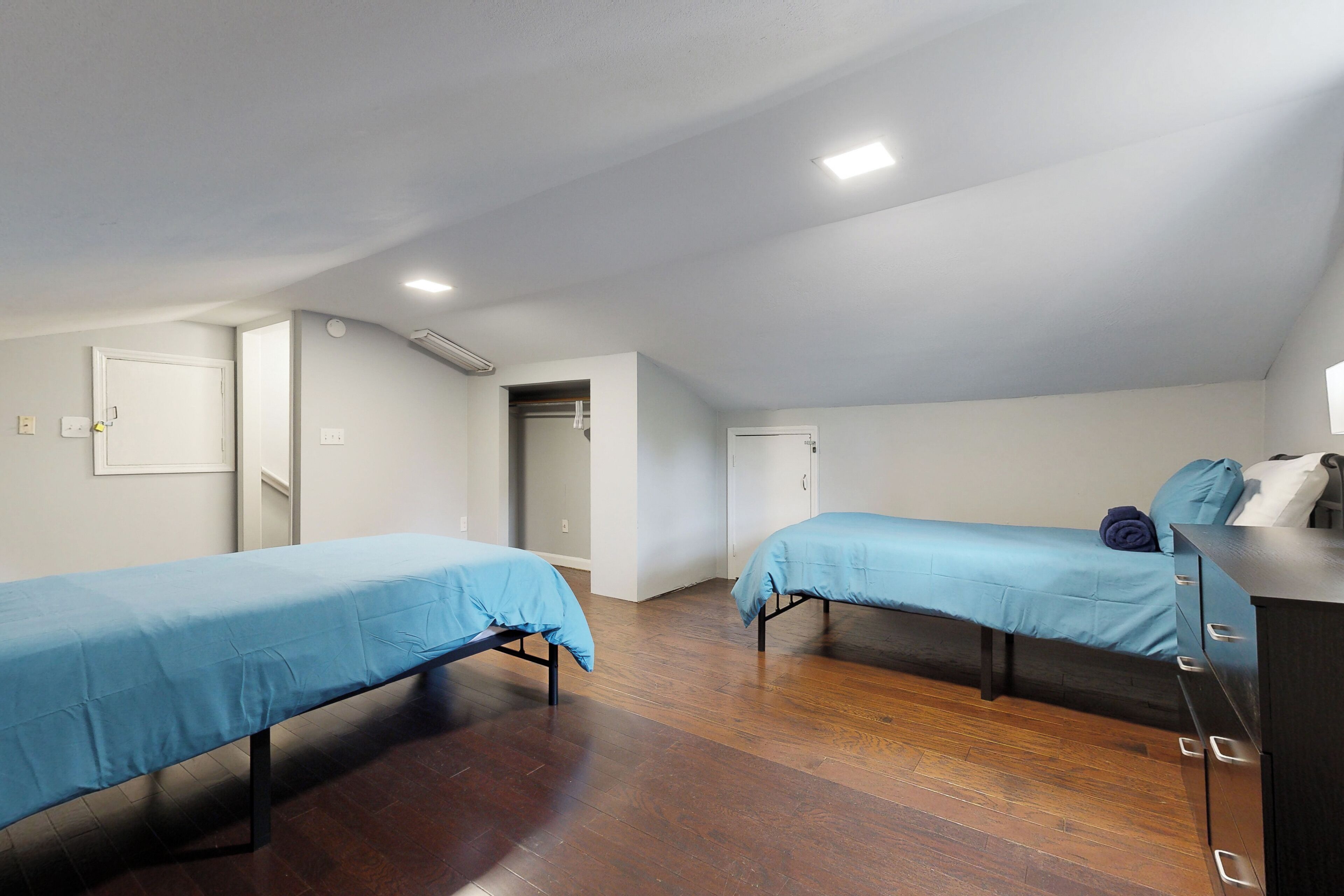 A room with two beds, wooden flooring, and a dresser with drawers.
