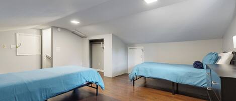 A room with two beds, wooden flooring, and a dresser with drawers.