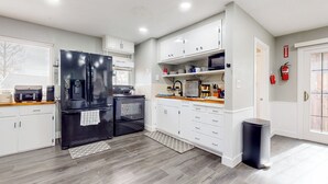 A modern kitchen with white cabinets, a black refrigerator, a microwave, and a stove. There is a trash can and a small rug on the floor. - 3BR Dog-friendly Home Near River w/ Fire Pit (Bethel Island)